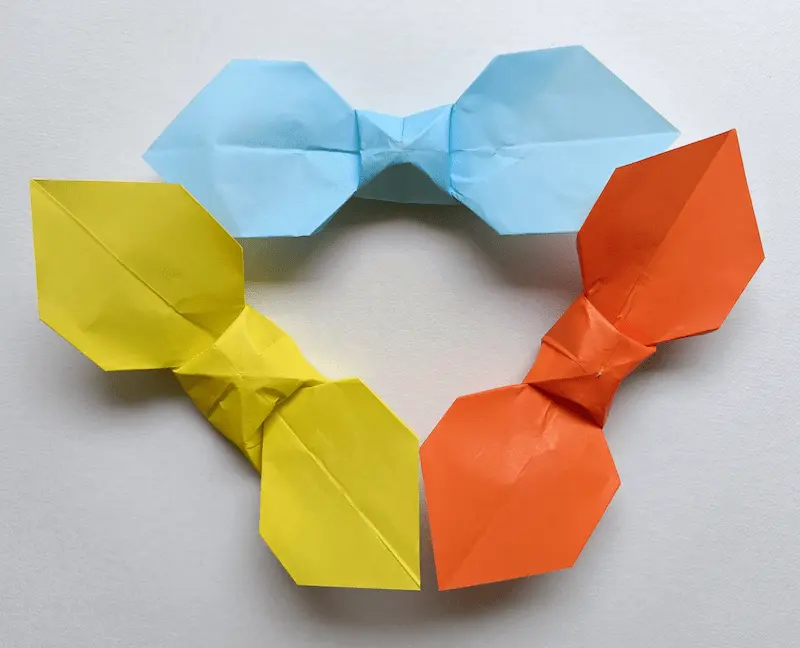 Real photos of three easy origami ribbons in different colors (orange, blue, and yellow) arranged in a triangle shape