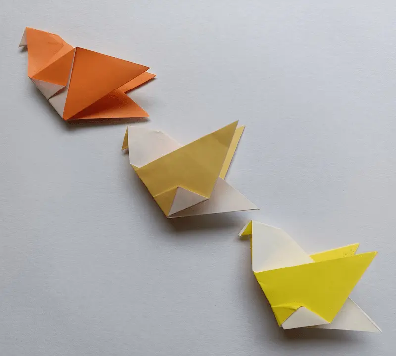 Three simple paper pigeons flying together in a diagonal line, shown in a real photo